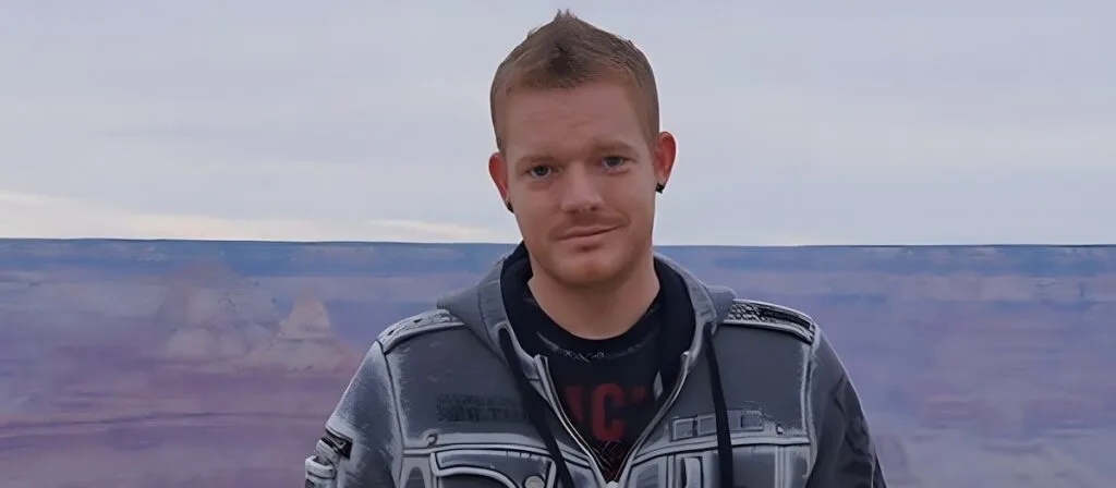 Terraria creator Andrew Spinks in a grey hoodie standing in front of a canyon landscape