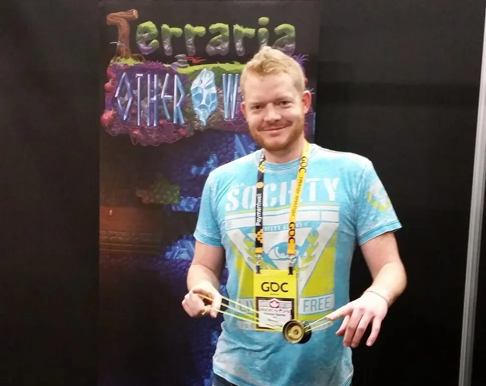 Andrew “Redigit” Spinks at GDC, wearing a conference badge in front of a Terraria: Otherworld banner