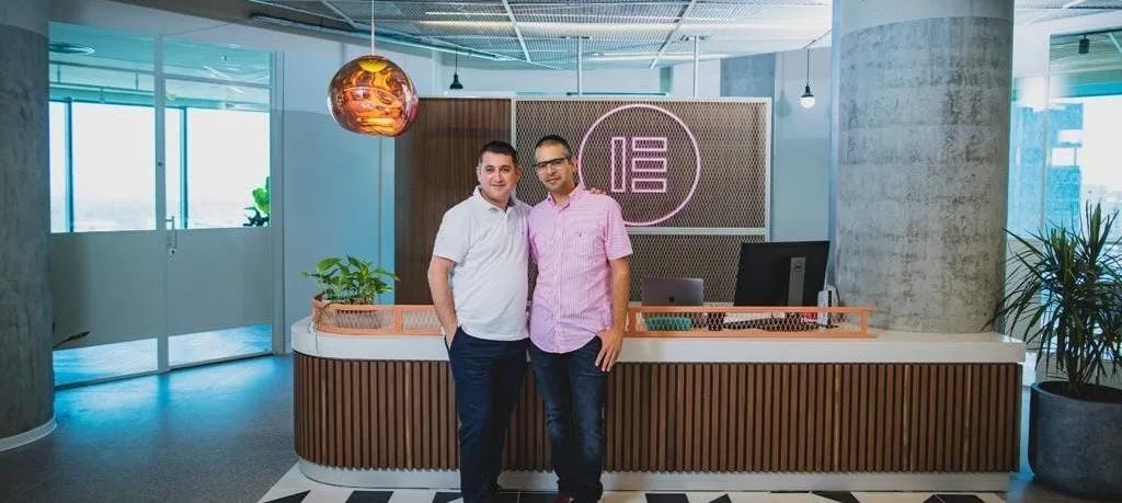 Elementor founders Yoni Luksenberg and Ariel Klikstein standing at their office reception under the Elementor logo